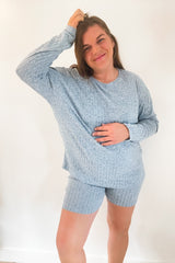 woman wearing a light blue maternity short pajama set, gently holding her baby bump