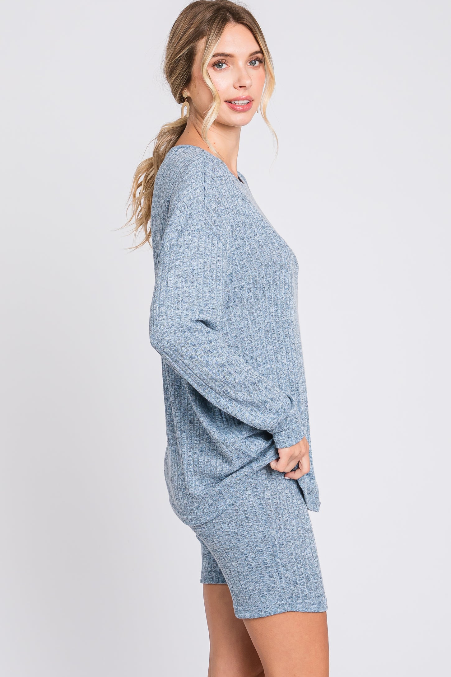 woman wearing a light blue ribbed sweater and matching shorts, posing sideways against a plain background