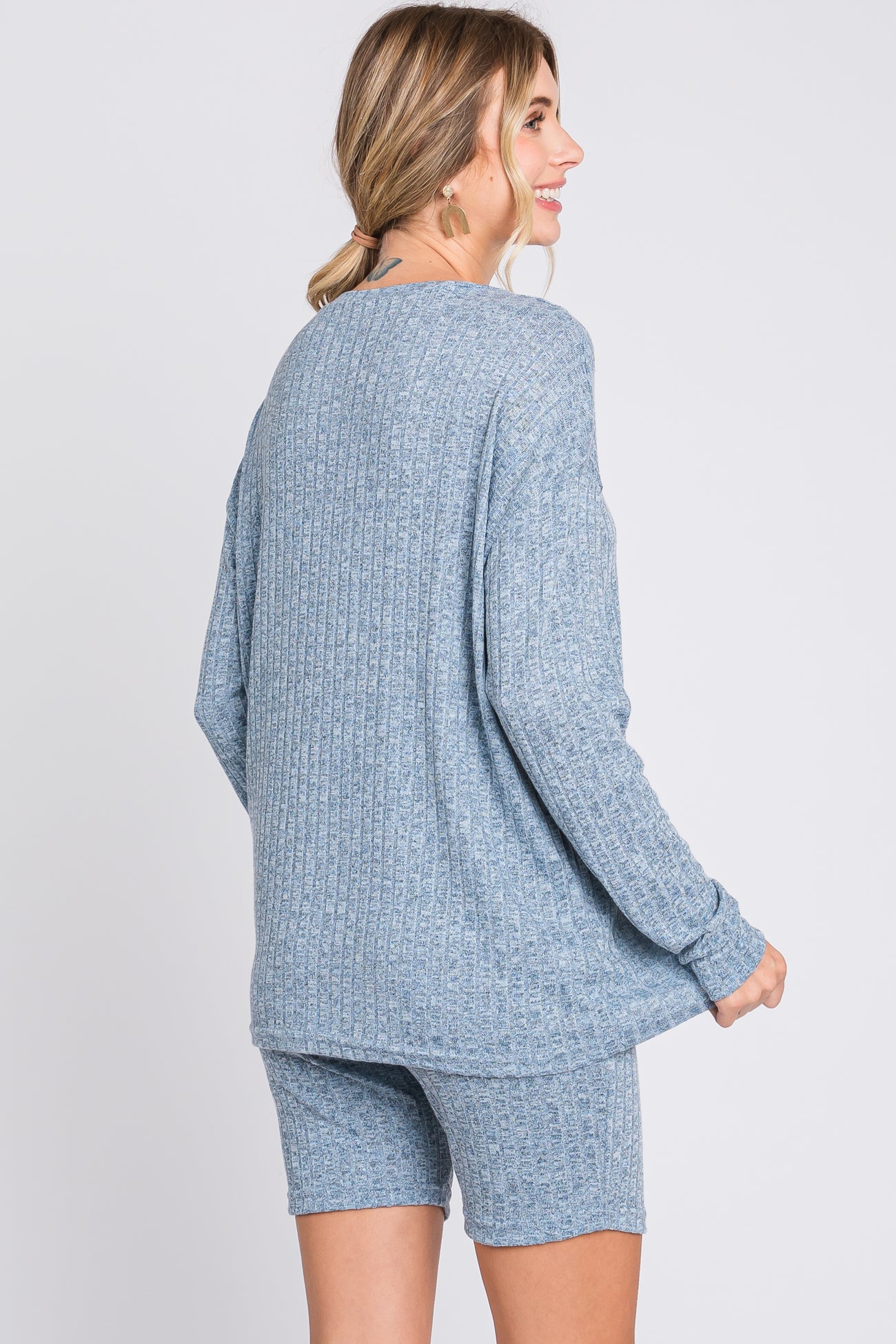 woman wearing a light blue ribbed sweater and matching shorts, facing slightly away from the camera
