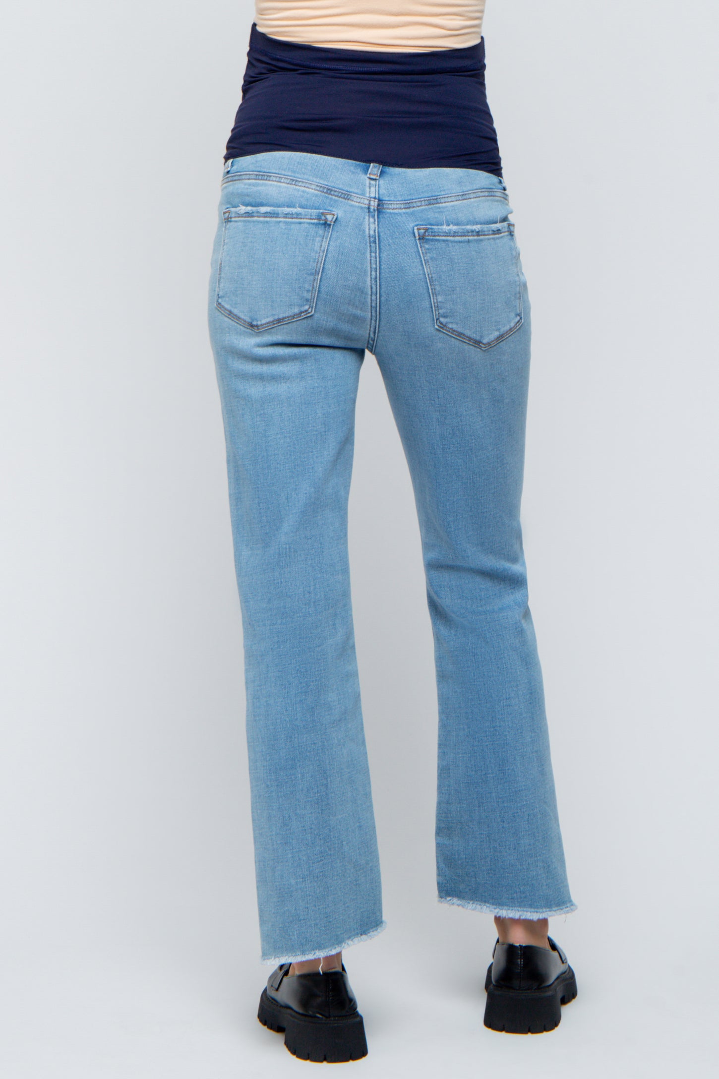 woman wearing light blue maternity jeans with a frayed hem and a ruched navy top, showing a baby bump