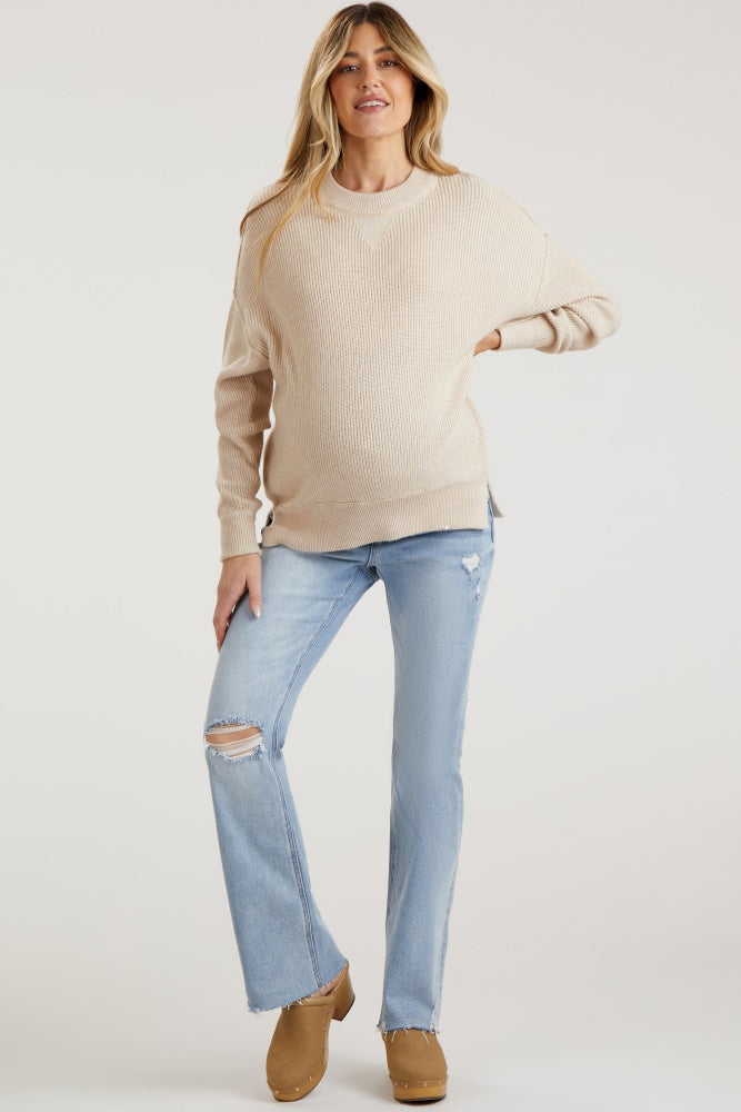 woman wearing a beige knit maternity sweater and distressed light blue jeans, showing her baby bump