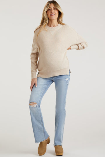woman wearing a beige knit maternity sweater and distressed light blue jeans, showing her baby bump