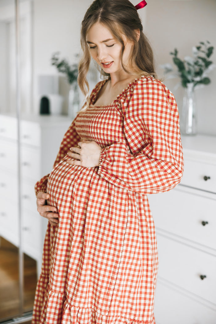 woman wearing a red and white checkered maternity dress, gently holding her baby bump