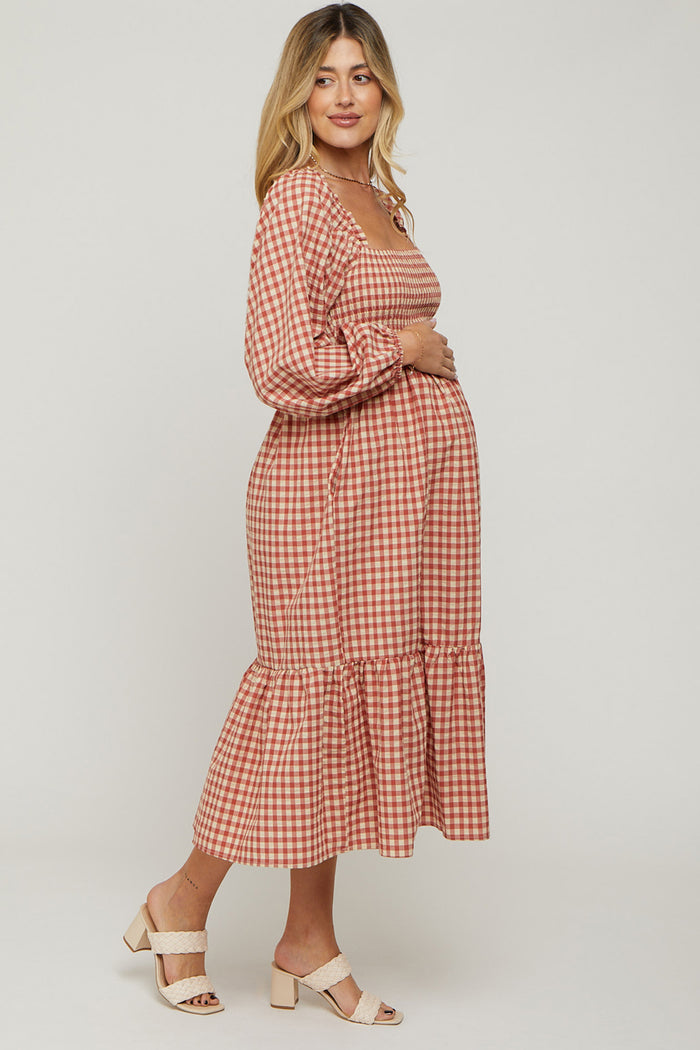 woman wearing a red and white checked maternity dress with a square neckline and ruffle hem, gently cradling her baby bump