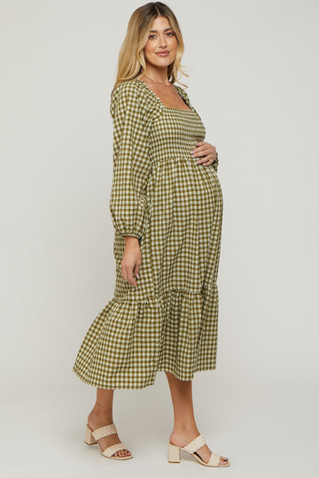 woman wearing a green and tan checked maternity dress with puff sleeves and a tiered skirt, holding her baby bump