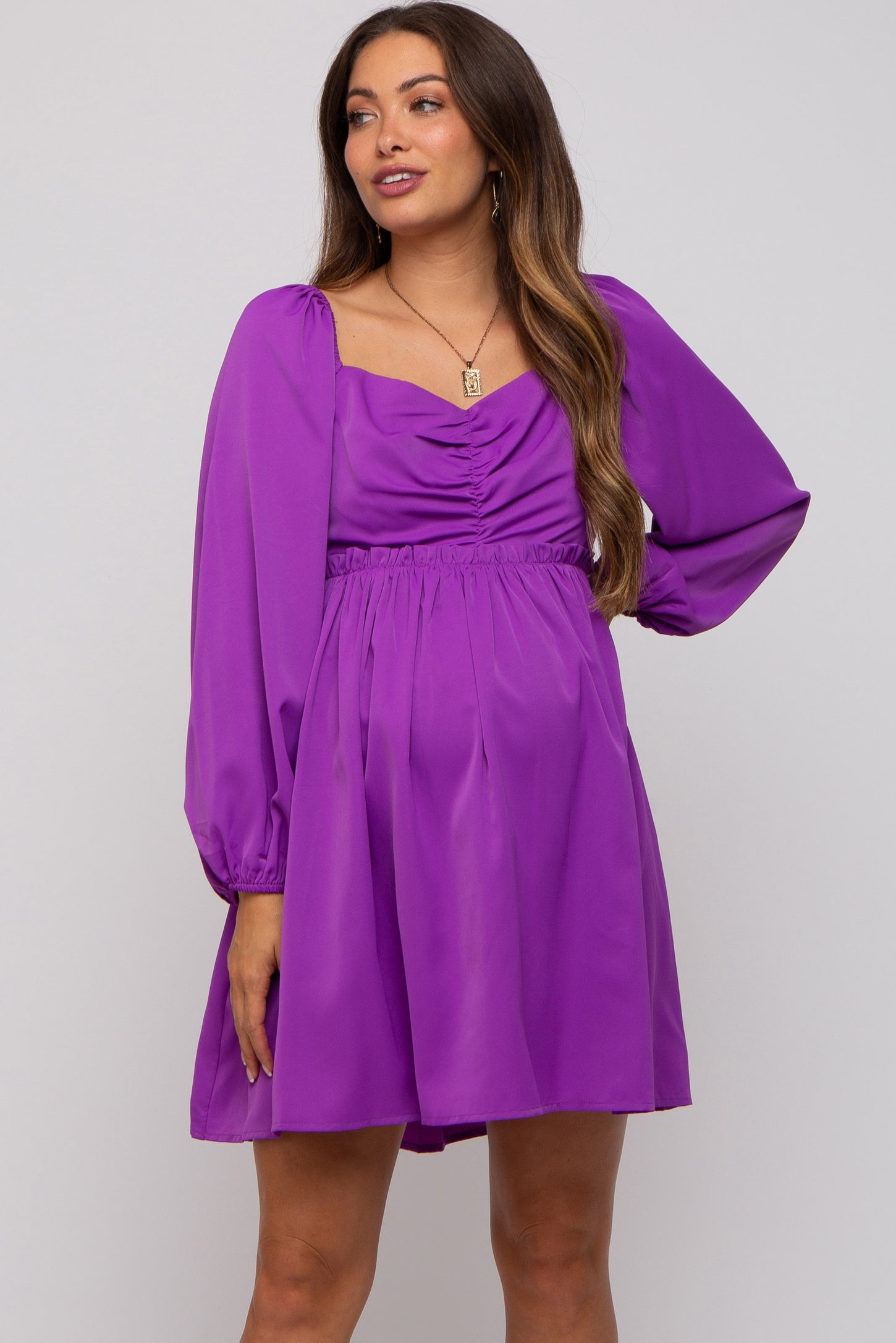woman wearing a purple maternity dress with long puff sleeves and a ruched bodice accentuating her baby bump