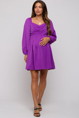 woman wearing a purple short sleeve maternity dress with a ruched bodice and holding her baby bump