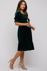 woman wearing a dark green velvet maternity dress with puff sleeves and a ruffled hem, showing her baby bump