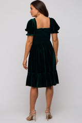 woman wearing a dark green velvet maternity dress with short puff sleeves and a ruffled hem, showing a baby bump