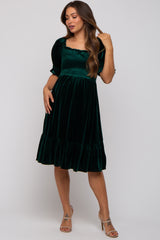 woman wearing a dark green velvet maternity dress with a square neckline and puff sleeves, showcasing her baby bump