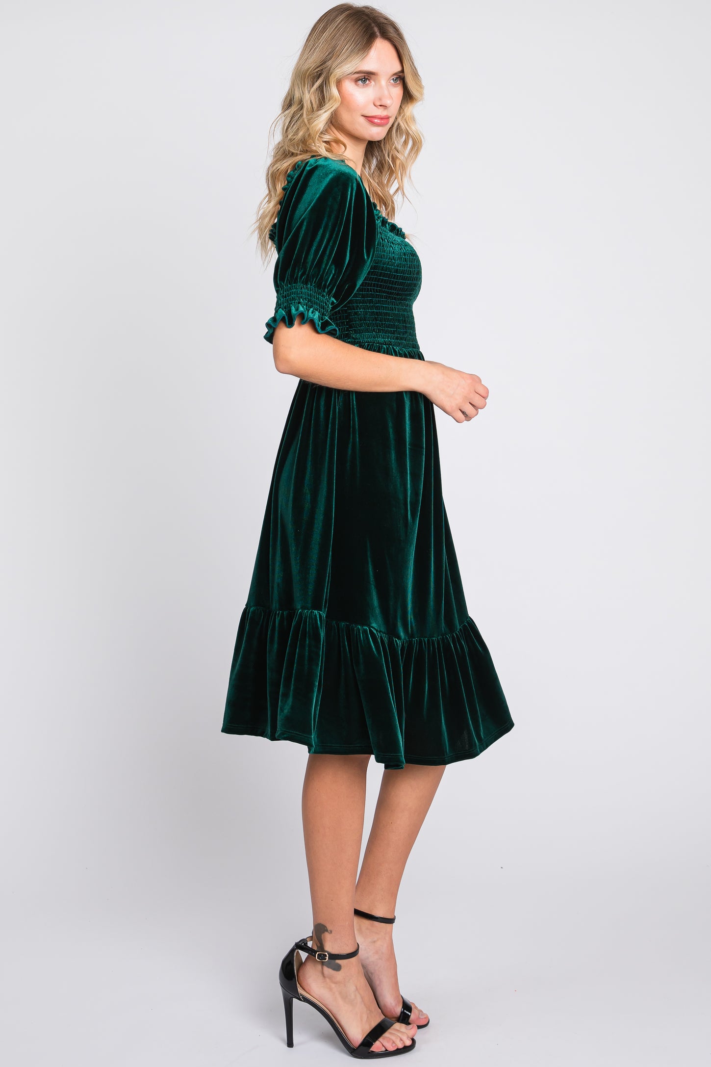 woman wearing a dark green velvet midi dress with puff sleeves and a ruffled hem