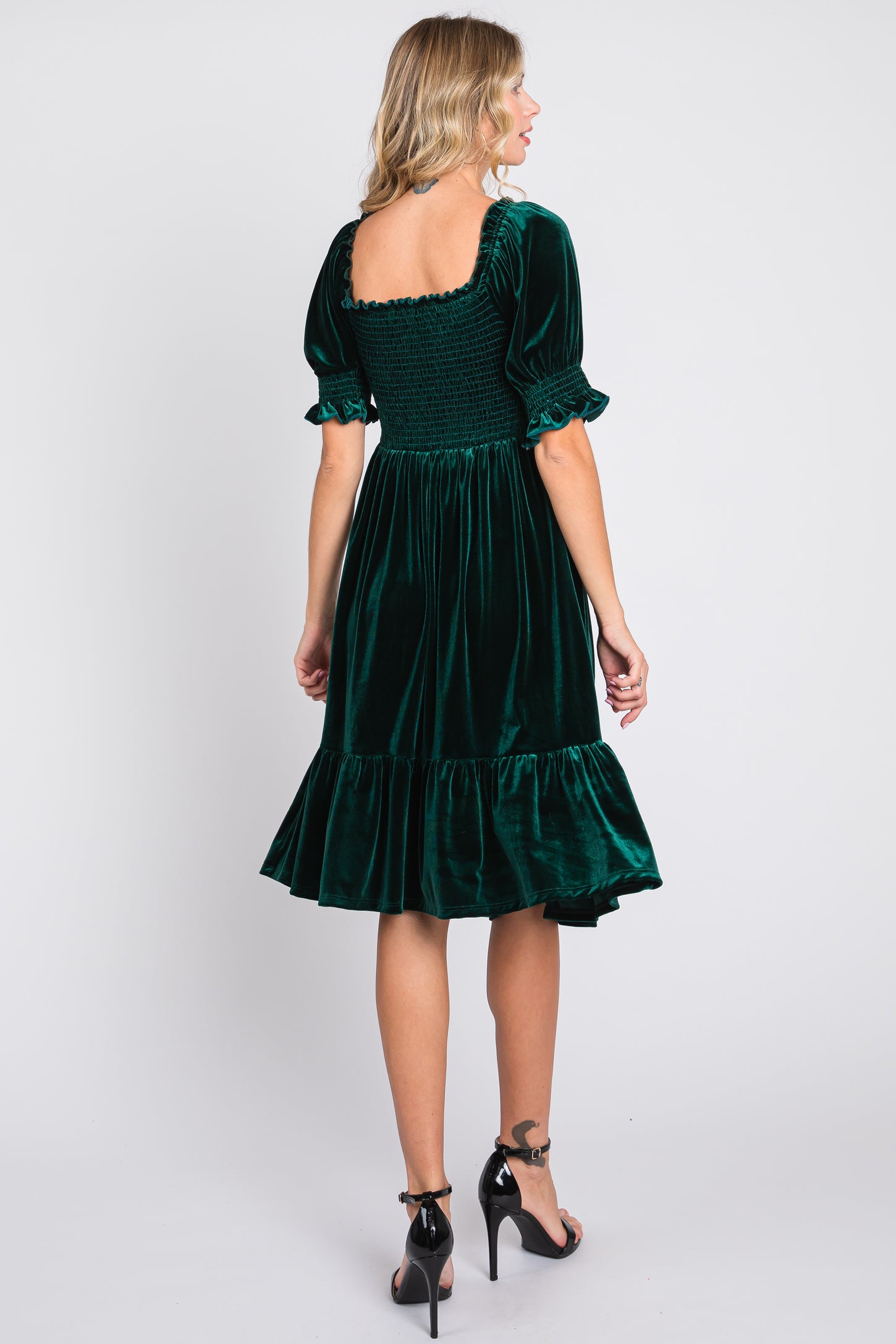 woman wearing a dark green velvet dress with puff sleeves and a tiered hem, viewed from the back