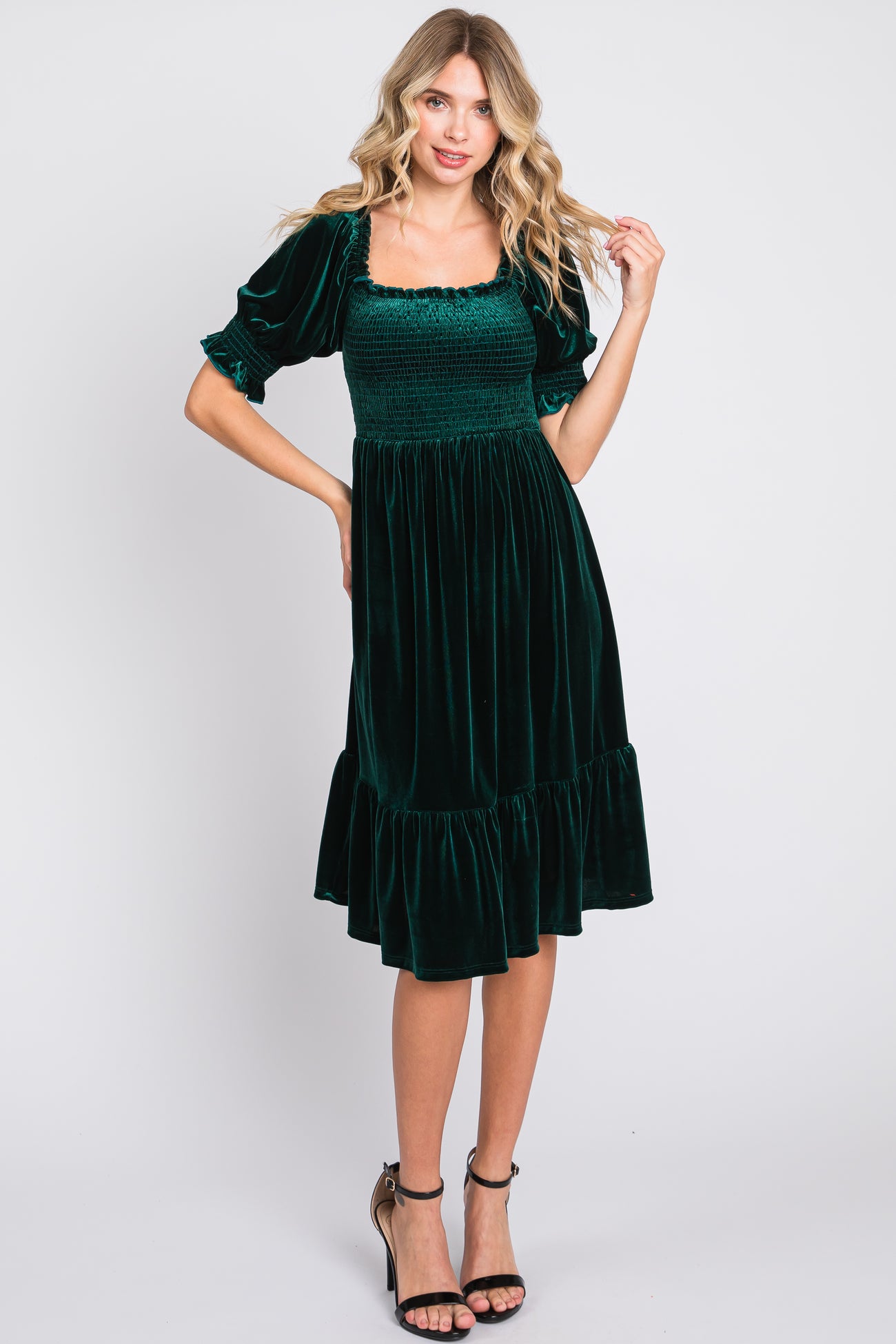 woman wearing a dark green velvet midi dress with puff sleeves and a ruffled hem
