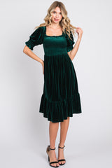 woman wearing a dark green velvet midi dress with puff sleeves and a ruffled hem
