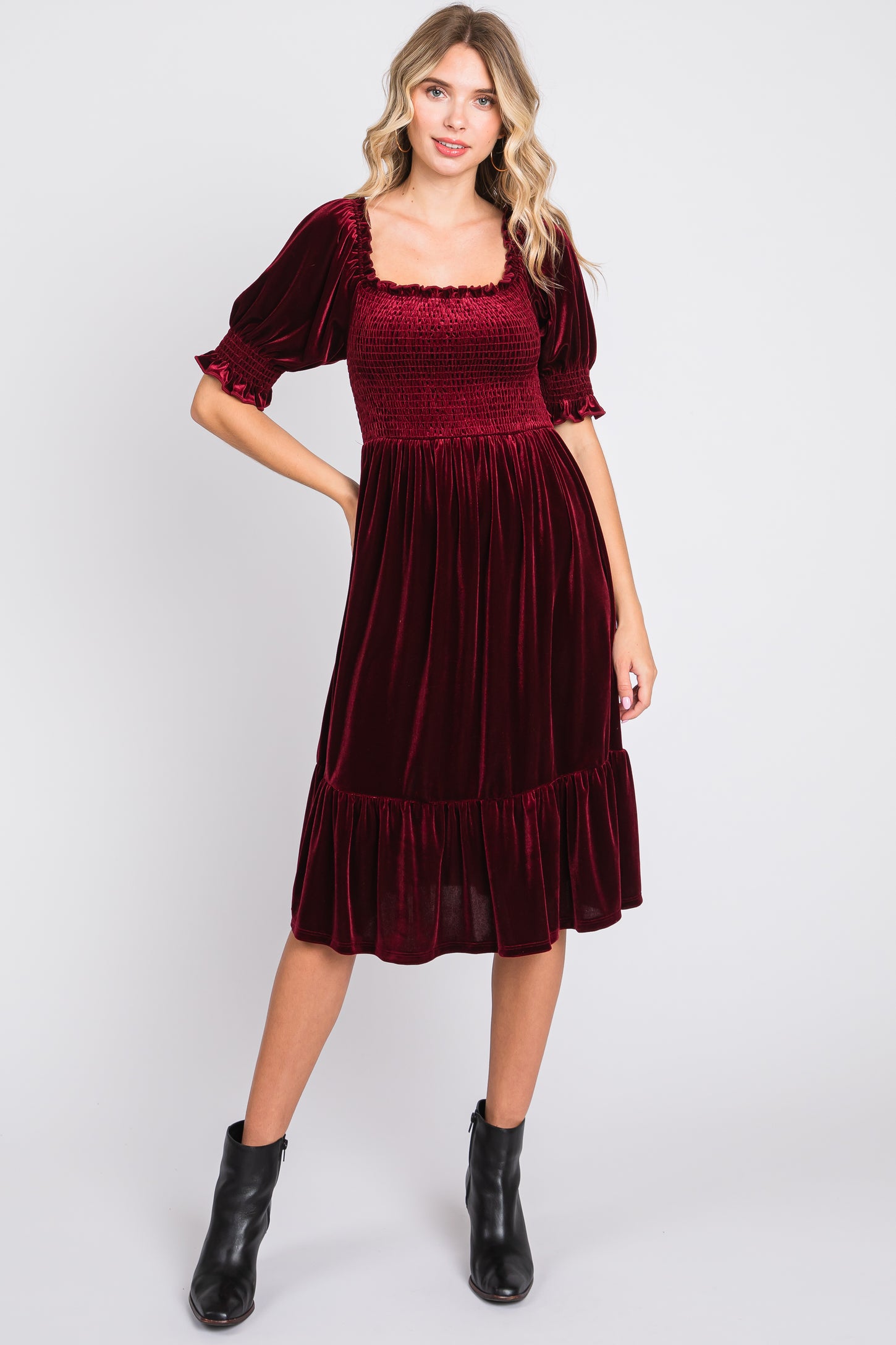 woman wearing a burgundy smocked velvet midi dress with puff sleeves and a ruffled hem