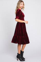woman wearing a burgundy velvet midi dress with smocked bodice and ruffled hem, paired with black ankle boots