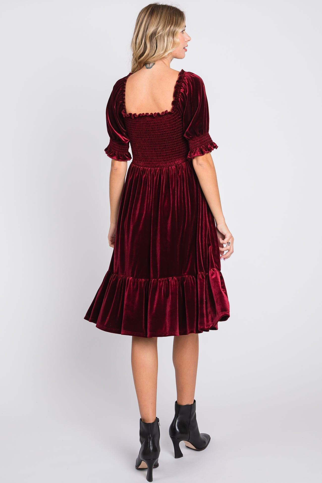 woman wearing a burgundy velvet puff sleeve dress with a smocked back and ruffled hem
