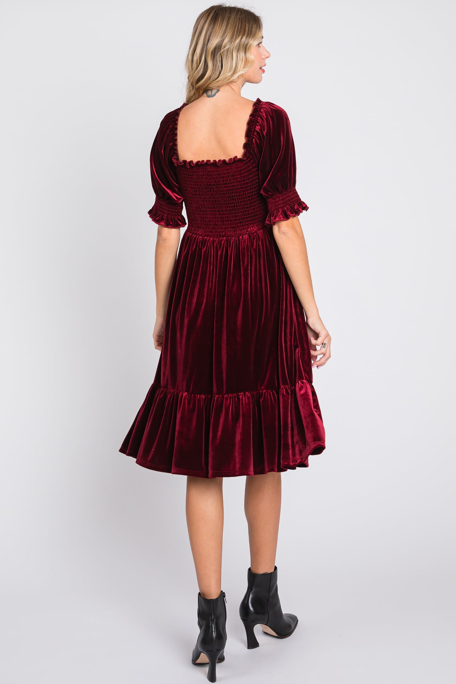 woman wearing a burgundy velvet puff sleeve dress with a smocked back and ruffled hem