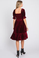woman wearing a burgundy velvet puff sleeve dress with a smocked back and ruffled hem