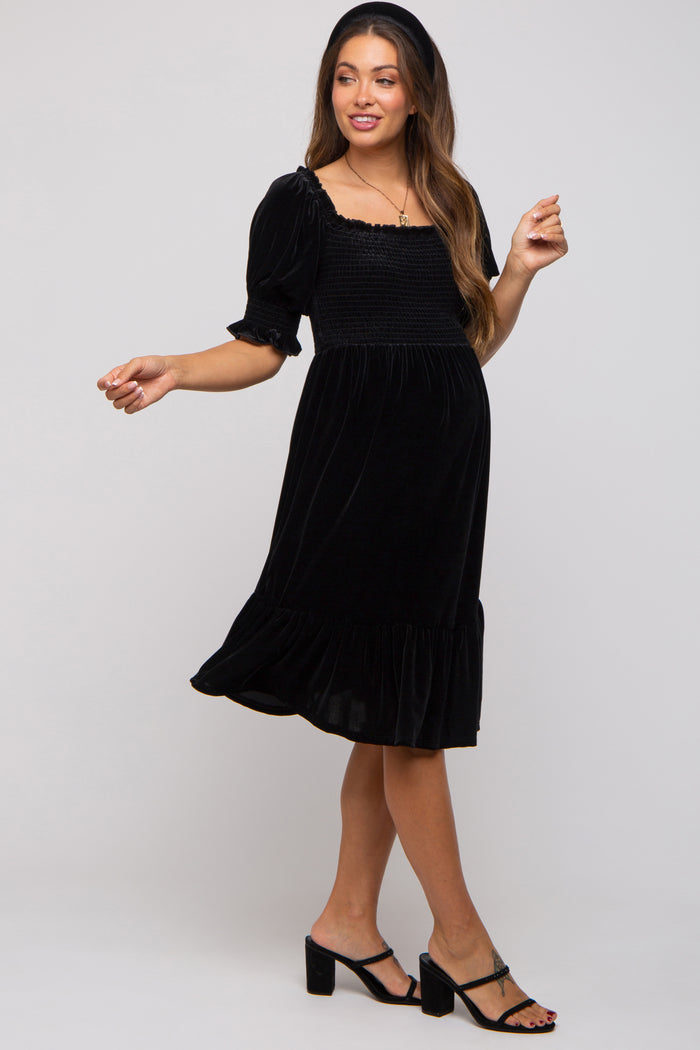woman wearing a black velvet maternity dress with short puff sleeves and a ruffled hem, showcasing her baby bump
