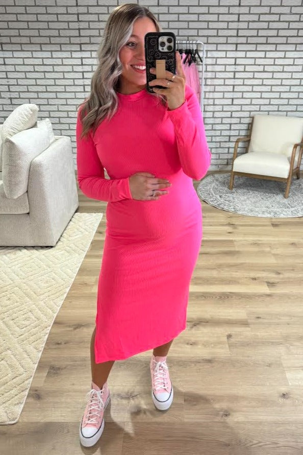 woman wearing a bright pink long sleeve maternity dress and showing her baby bump while taking a selfie in a mirror