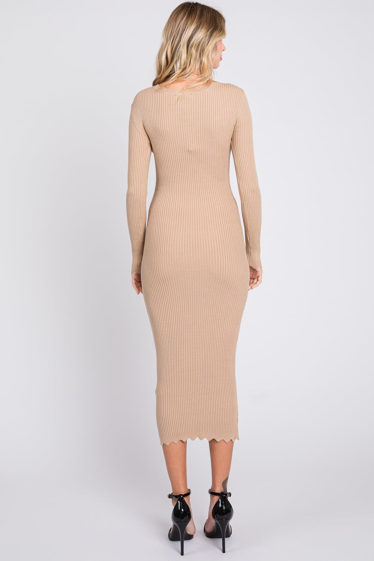woman wearing a beige ribbed midi dress with long sleeves and a scalloped hem, standing with her back to the camera