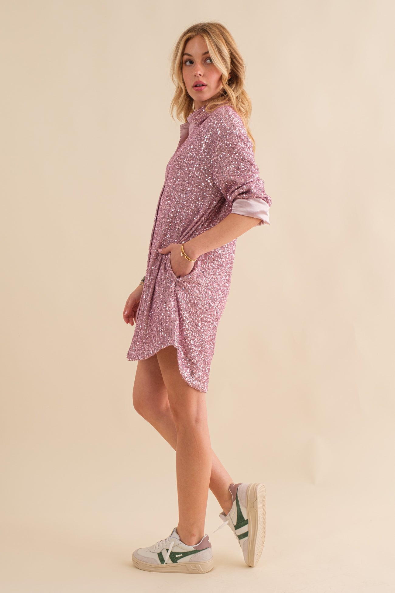 woman wearing a pink sequin shirt dress with rolled sleeves and pockets, styled with white sneakers
