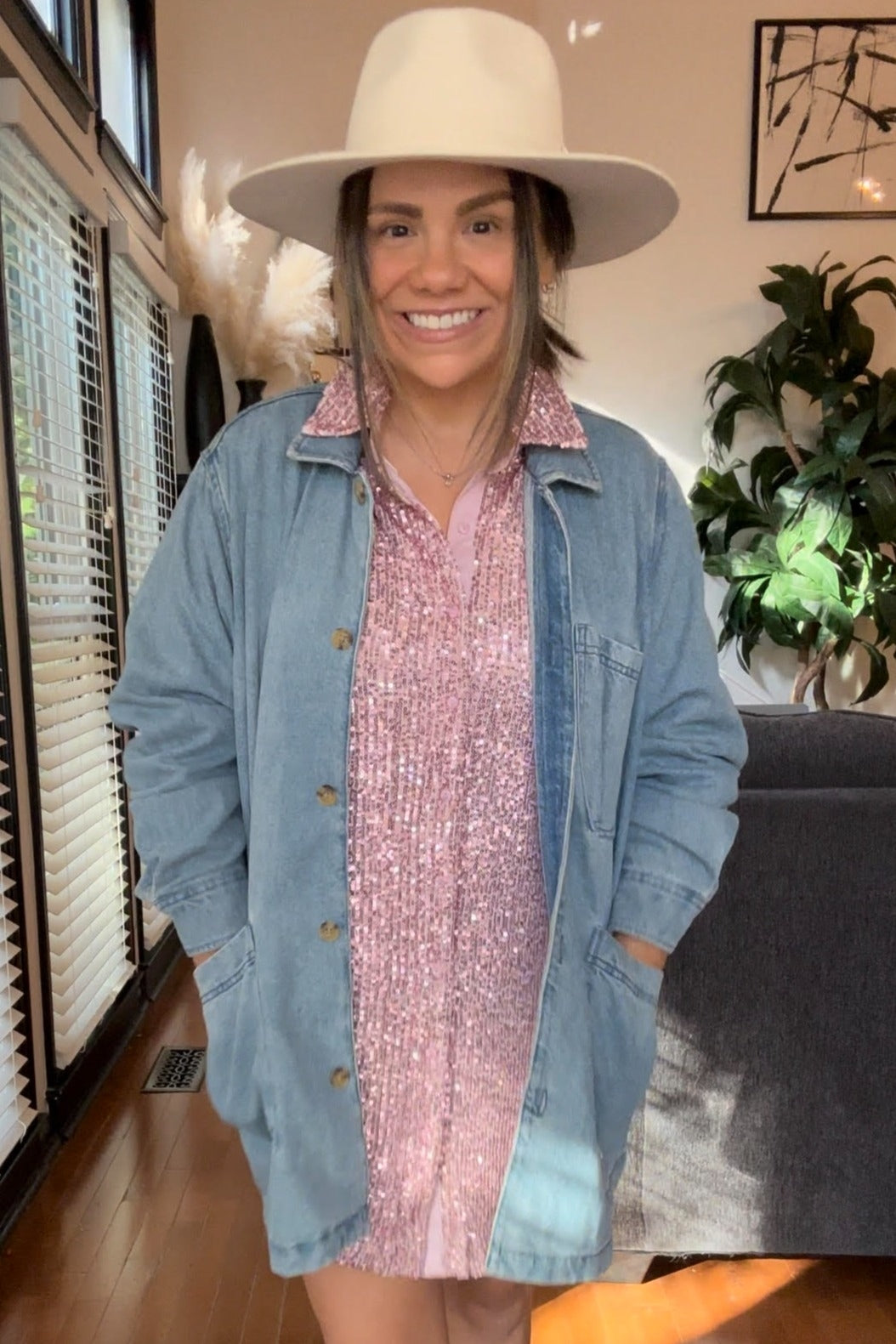 woman wearing a denim jacket over a pink sequin dress, styled with a white wide-brimmed hat