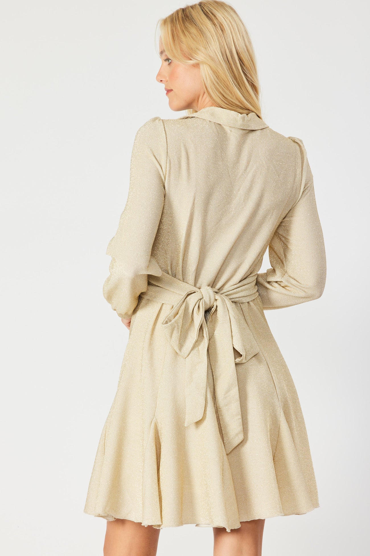 woman wearing a beige belted dress with a flared skirt and long sleeves, shown from the back