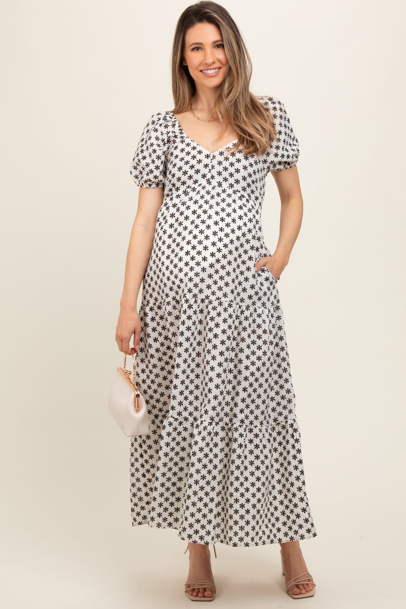 woman wearing a black and white floral print maternity dress with puff sleeves and pockets, holding a small clutch
