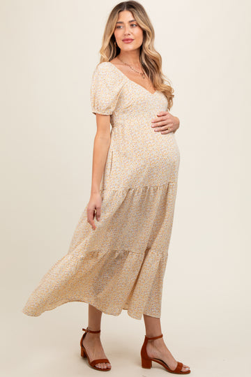 woman wearing a light yellow floral maternity maxi dress and holding her baby bump