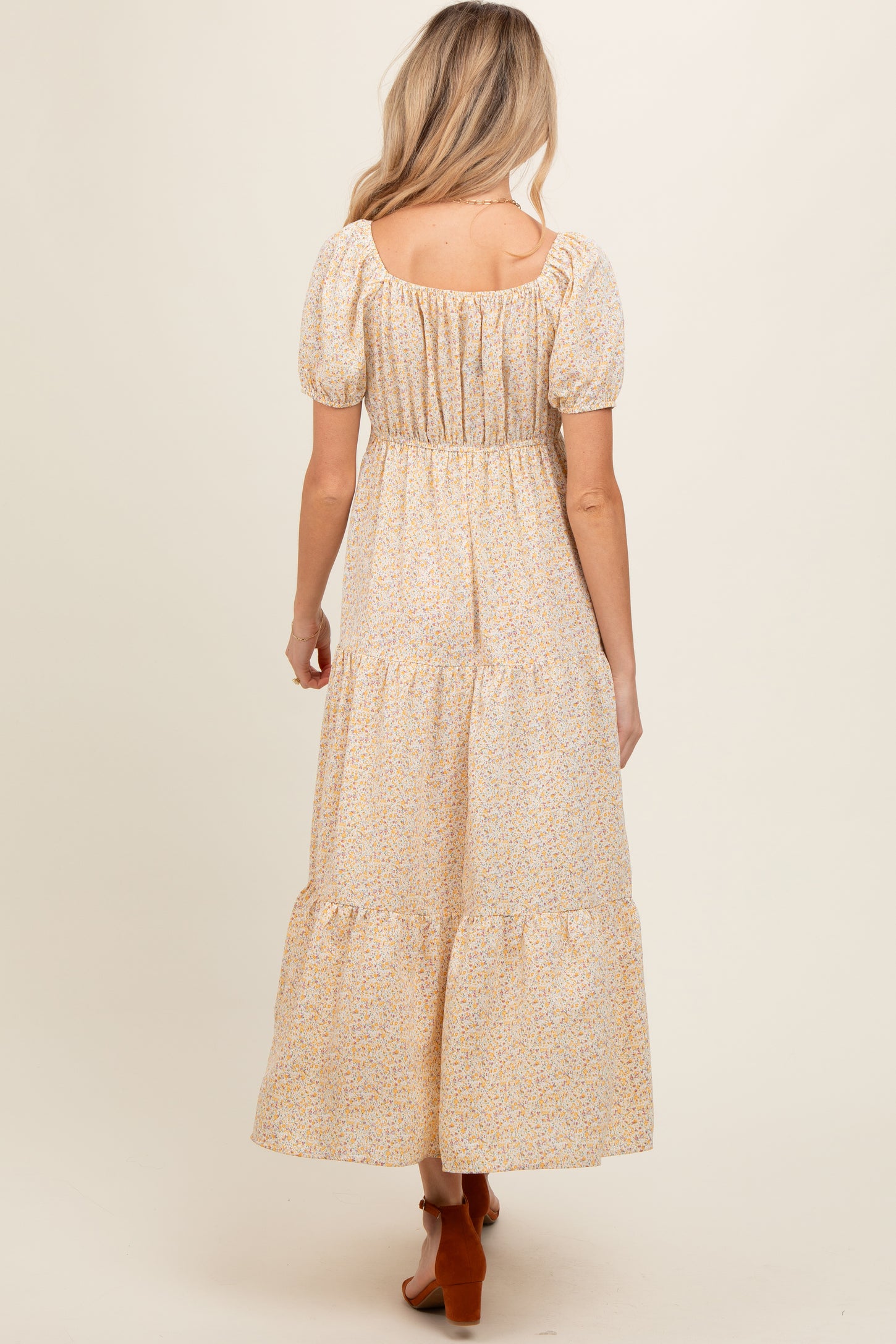 woman wearing a yellow floral maternity maxi dress with puffed sleeves and tiered hem, showing her back
