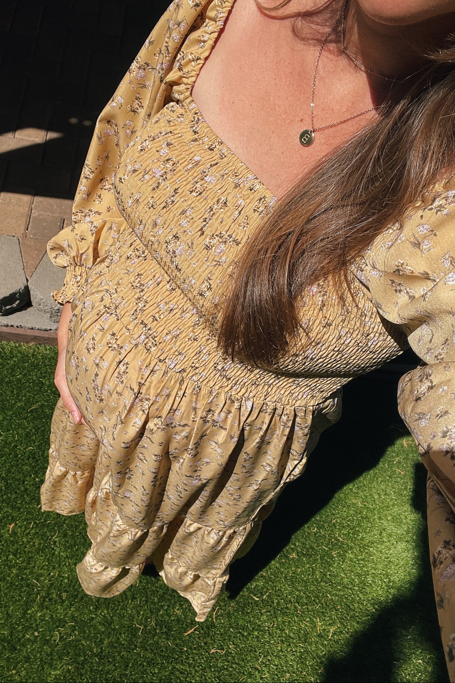 woman wearing a yellow floral maternity dress with a smocked bodice and long sleeves, holding her baby bump