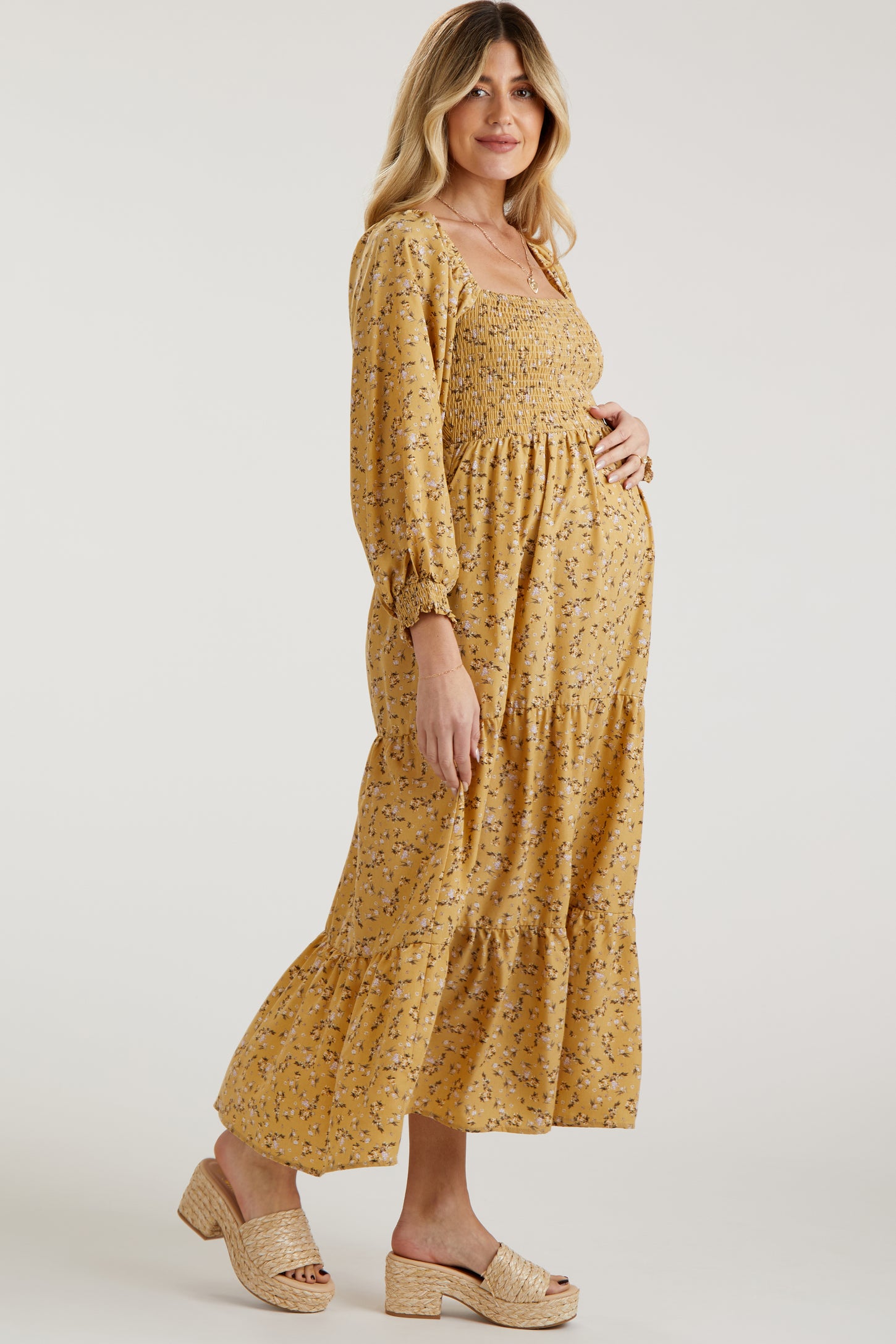 woman wearing a yellow floral maternity dress with smocked bodice and long sleeves, showing her baby bump
