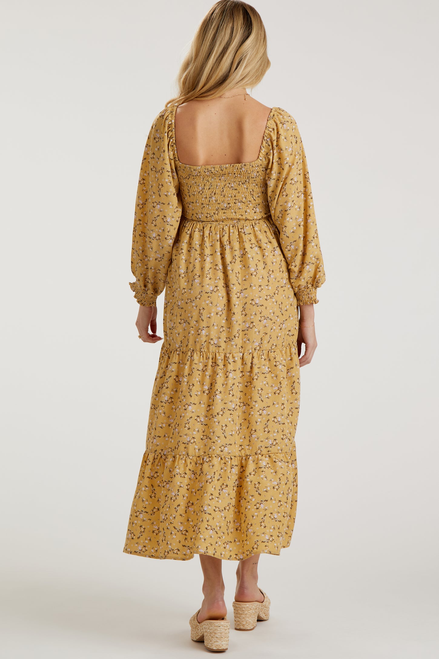 woman wearing a yellow floral maternity maxi dress with a smocked bodice and puffed sleeves, showing the back view