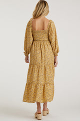 woman wearing a yellow floral maternity maxi dress with a smocked bodice and puffed sleeves, showing the back view
