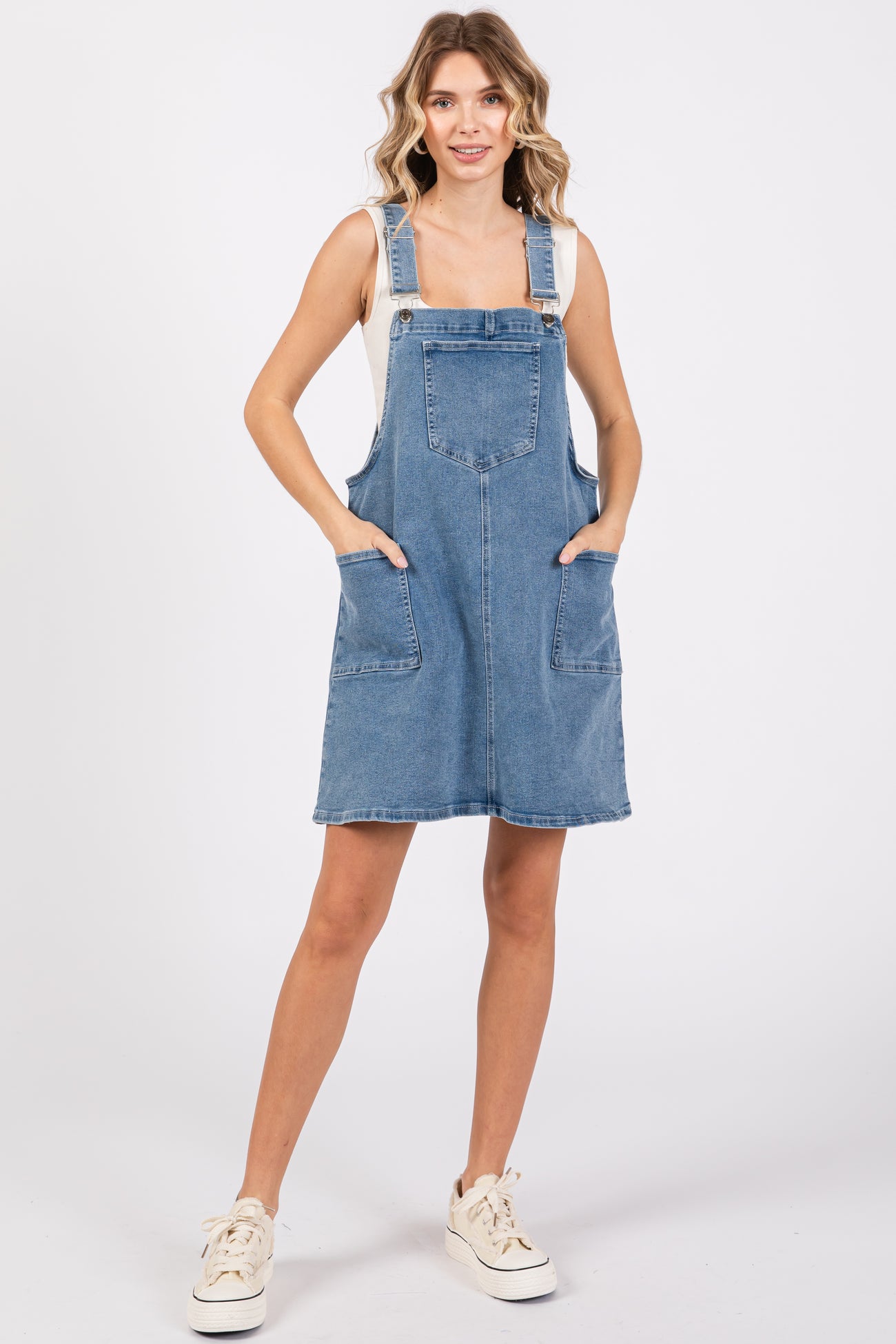 woman wearing a denim overall dress with large front pockets and a relaxed fit, paired with a light top and sneakers