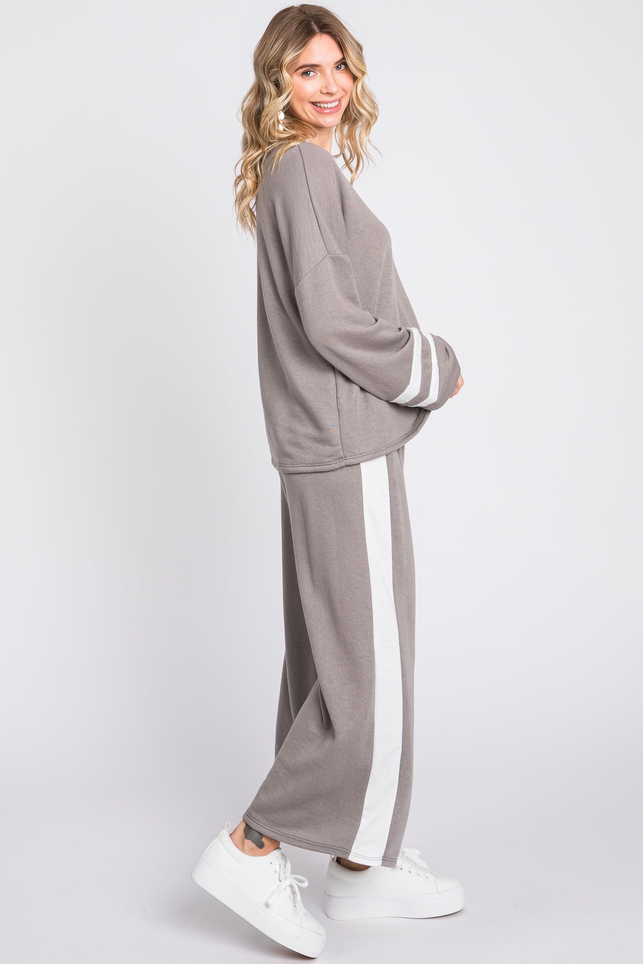 woman wearing a gray lounge set with white stripes on the pants and long sleeves, paired with white sneakers
