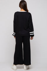 woman wearing a black maternity sweater with white stripes on the sleeves and matching black wide-leg pants