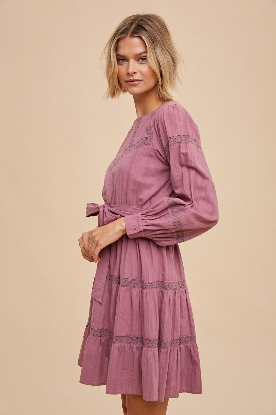 woman wearing a dusty rose long sleeve dress with lace details and a tie waist