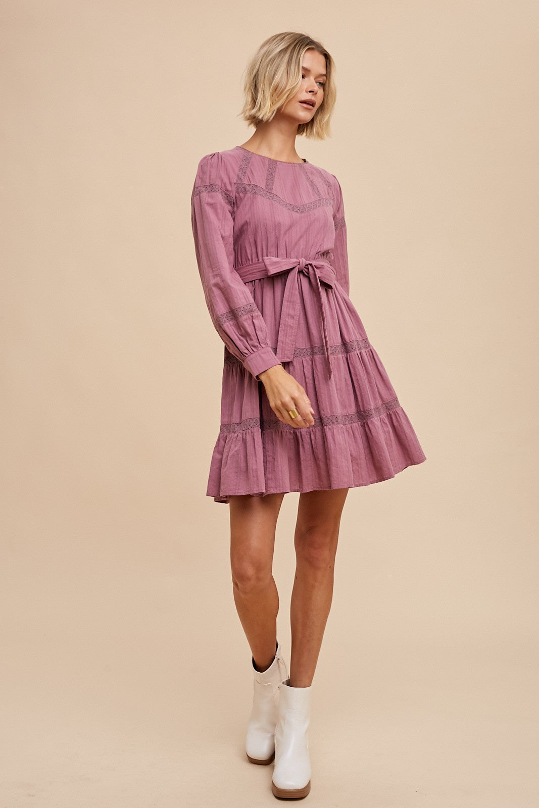 woman wearing a dusty rose long sleeve dress with a belt and tiered ruffles, styled with white ankle boots
