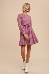 woman wearing a dusty rose long sleeve dress with a belt and tiered ruffles, styled with white ankle boots