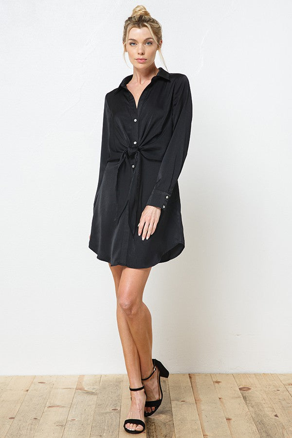 woman wearing a black long sleeve button-up dress with a knot detail at the waist and strappy black heels
