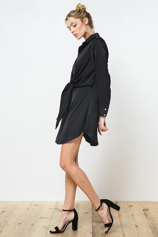 woman wearing a black long sleeve shirt dress with a tied waist and side slits, paired with black high heel sandals