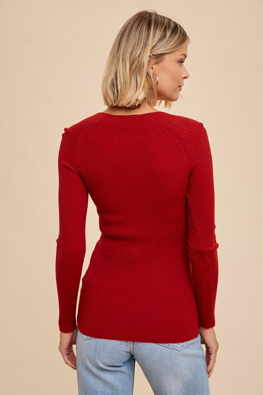 woman wearing a red ribbed knit long sleeve sweater, shown from the back with worn light blue jeans