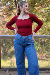 woman wearing a ribbed red long sleeve top with a scooped neckline and high-waisted blue jeans, standing outdoors