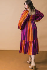 woman wearing a multicolored striped plus-size dress with puff sleeves and a tiered skirt, view from the back