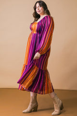 woman wearing a colorful striped plus-size maxi dress with long sleeves and a tiered hem, styled with beige ankle boots