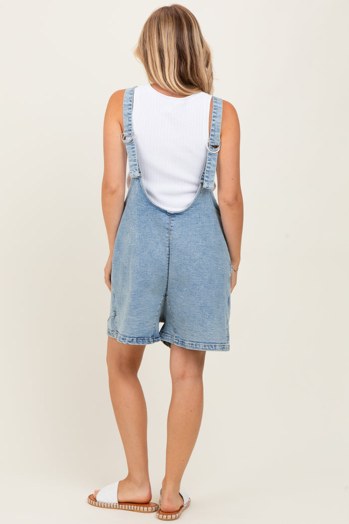 woman wearing a white tank top and denim overalls, showing the back view with light wash fabric and rolled cuffs