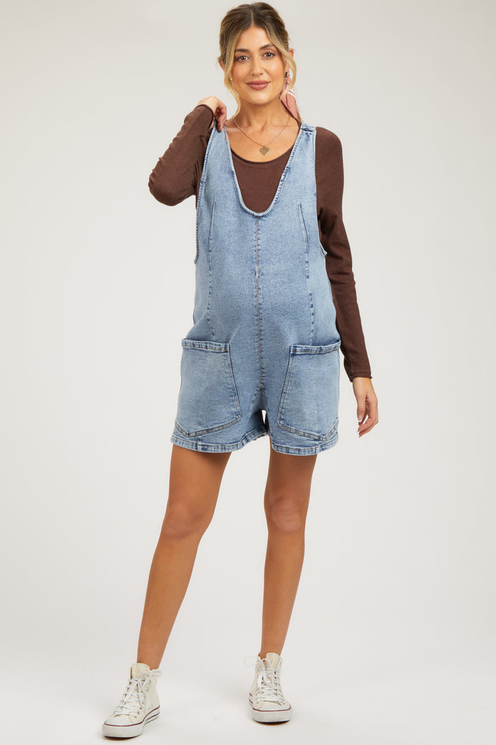 woman wearing a light blue maternity denim overall shorts and a brown long sleeve top, showcasing her baby bump